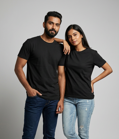 A man and a woman modeling plain black short-sleeve crewneck t-shirts, paired with blue jeans and white sneakers, against a solid light gray studio background.